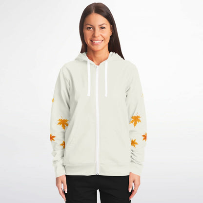 A woman modeling a light sage green zip-up hoodie with white drawstrings and orange maple leaf prints on the sleeves, set against a plain white studio background.