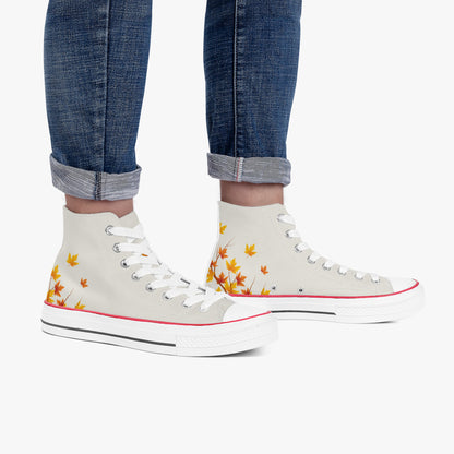 A pair of high-top canvas sneakers with a cream base, decorated with orange and yellow autumn maple leaves on the sides. The shoes are modeled with cuffed blue jeans against a clean white background.