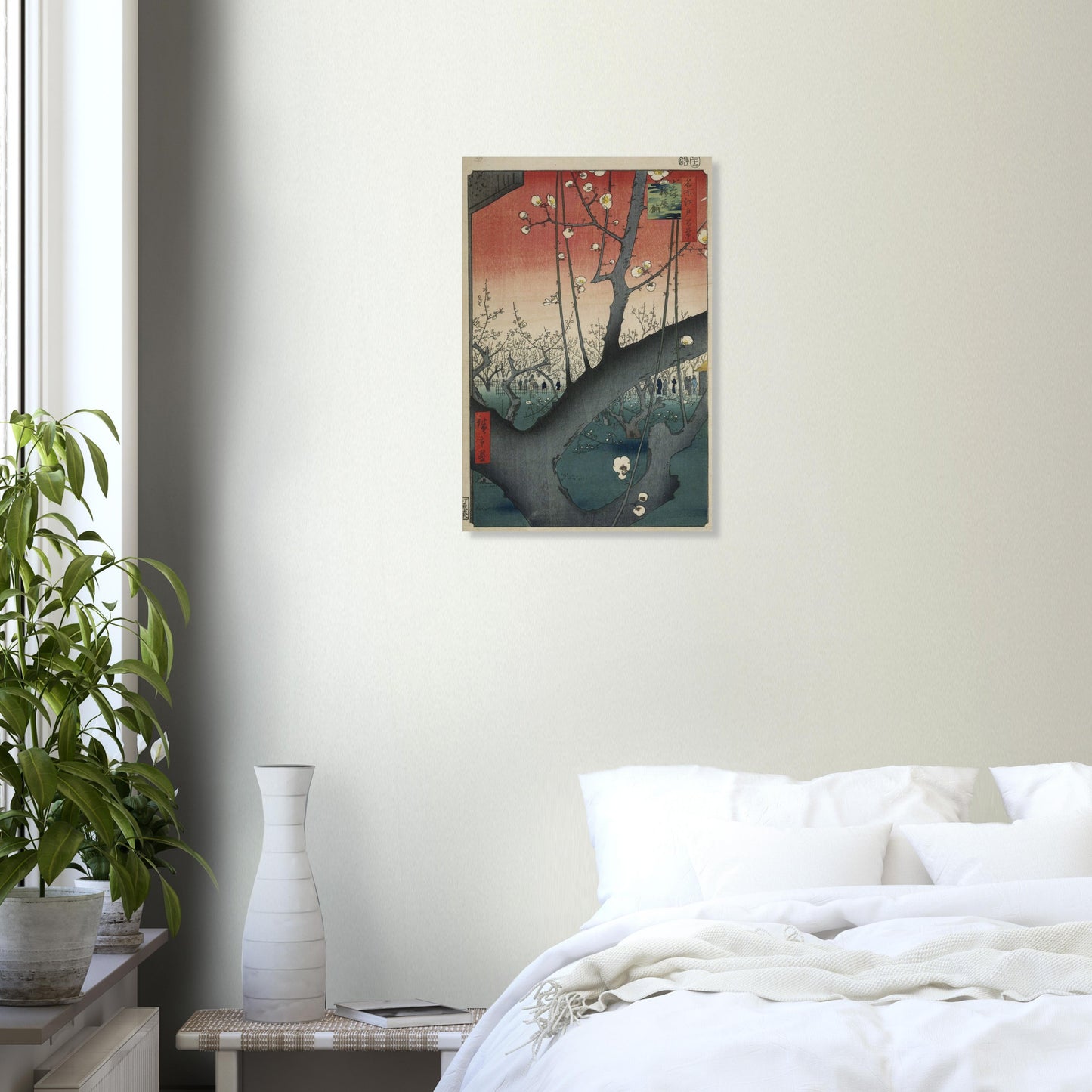 Framed artwork on a wall above a bed in a bedroom with a plant and vase.