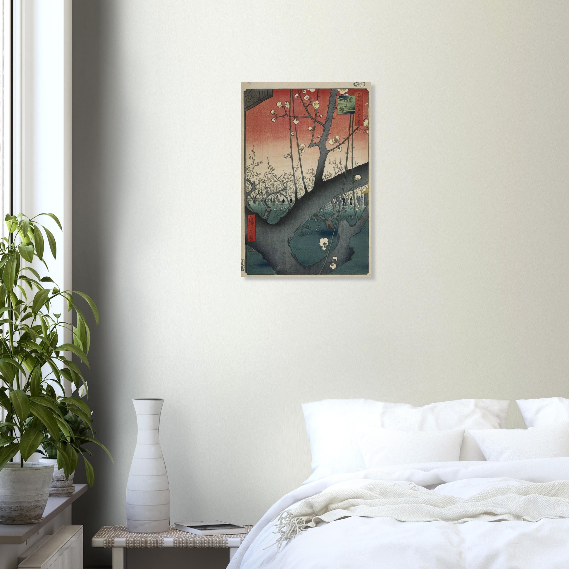 Framed artwork on a wall above a bed in a bedroom with a plant and vase.