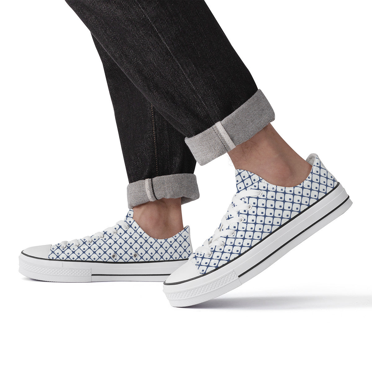 White slip-on sneakers with black geometric pattern worn with rolled-up jeans on a white background