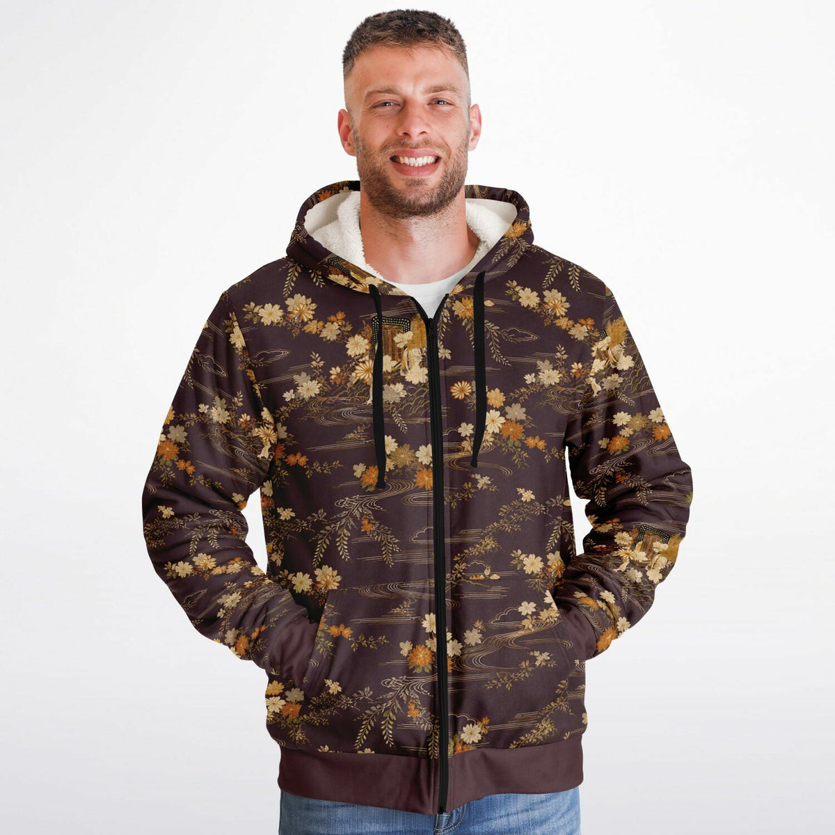 A man wearing a brown zip-up hoodie with a beige and gold floral pattern, featuring a white-lined hood and black drawstrings, set against a plain white background.