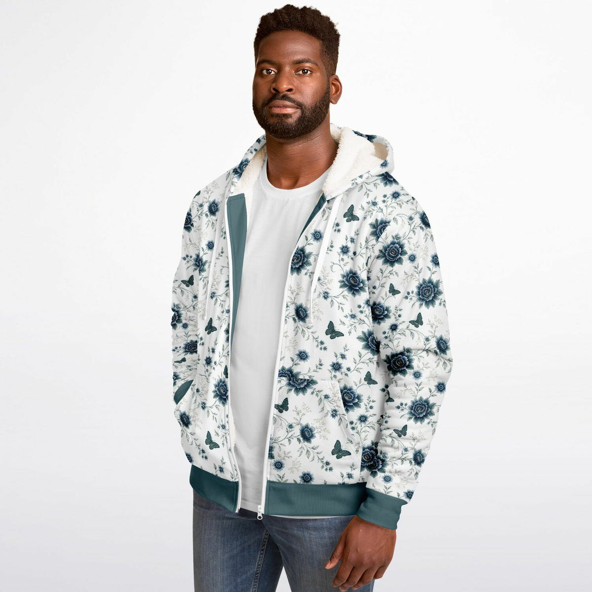 A man wearing a white hooded jacket with a dark teal floral and butterfly pattern, layered over a white t-shirt and blue jeans, against a plain white studio background.