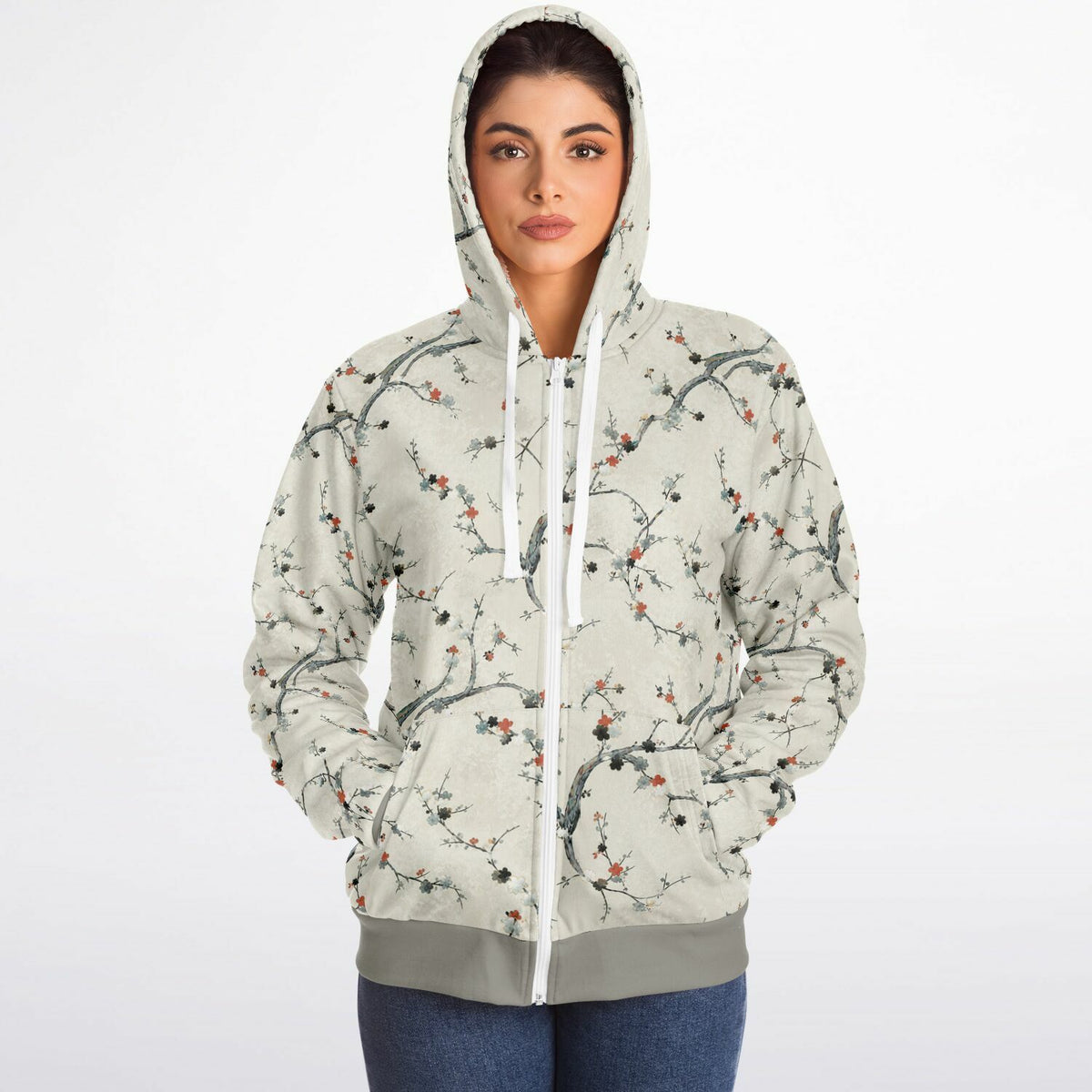 A woman wearing a light beige zip-up hoodie with a delicate branch and blossom print, paired with blue jeans, photographed against a clean white background.