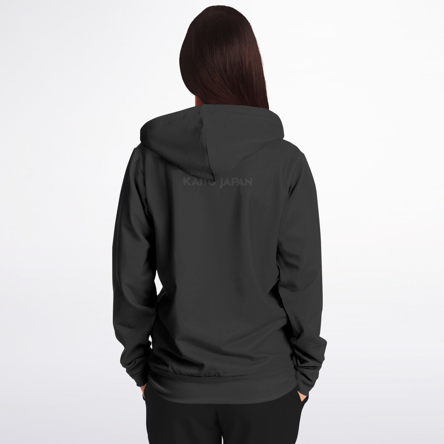 A woman viewed from the back wearing a dark charcoal gray hoodie with a subtle 'KAHOJAPAN' logo printed across the upper back, set against a plain light gray studio background.