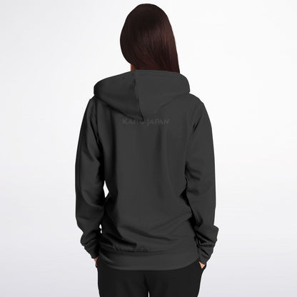 A woman viewed from the back wearing a dark charcoal gray hoodie with a subtle 'KAHOJAPAN' logo printed across the upper back, set against a plain light gray studio background.