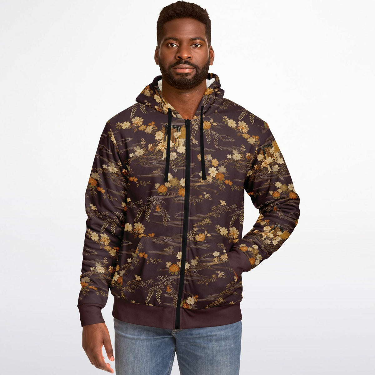 A man wearing a dark brown and black zip-up hoodie with a beige and gold floral pattern, paired with blue jeans, against a plain white background.