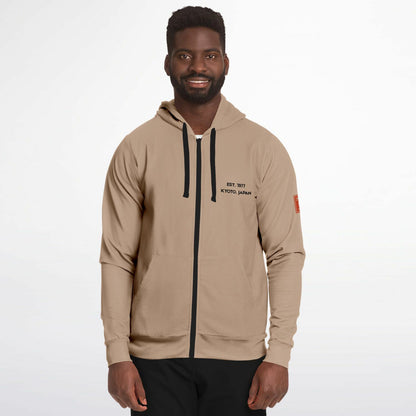 A man wearing a beige zip-up hoodie with black drawstrings, black text on the left chest reading 'EST. 2017 KYOYO JAPAN', and a small orange patch on the sleeve, photographed against a light gray studio background.