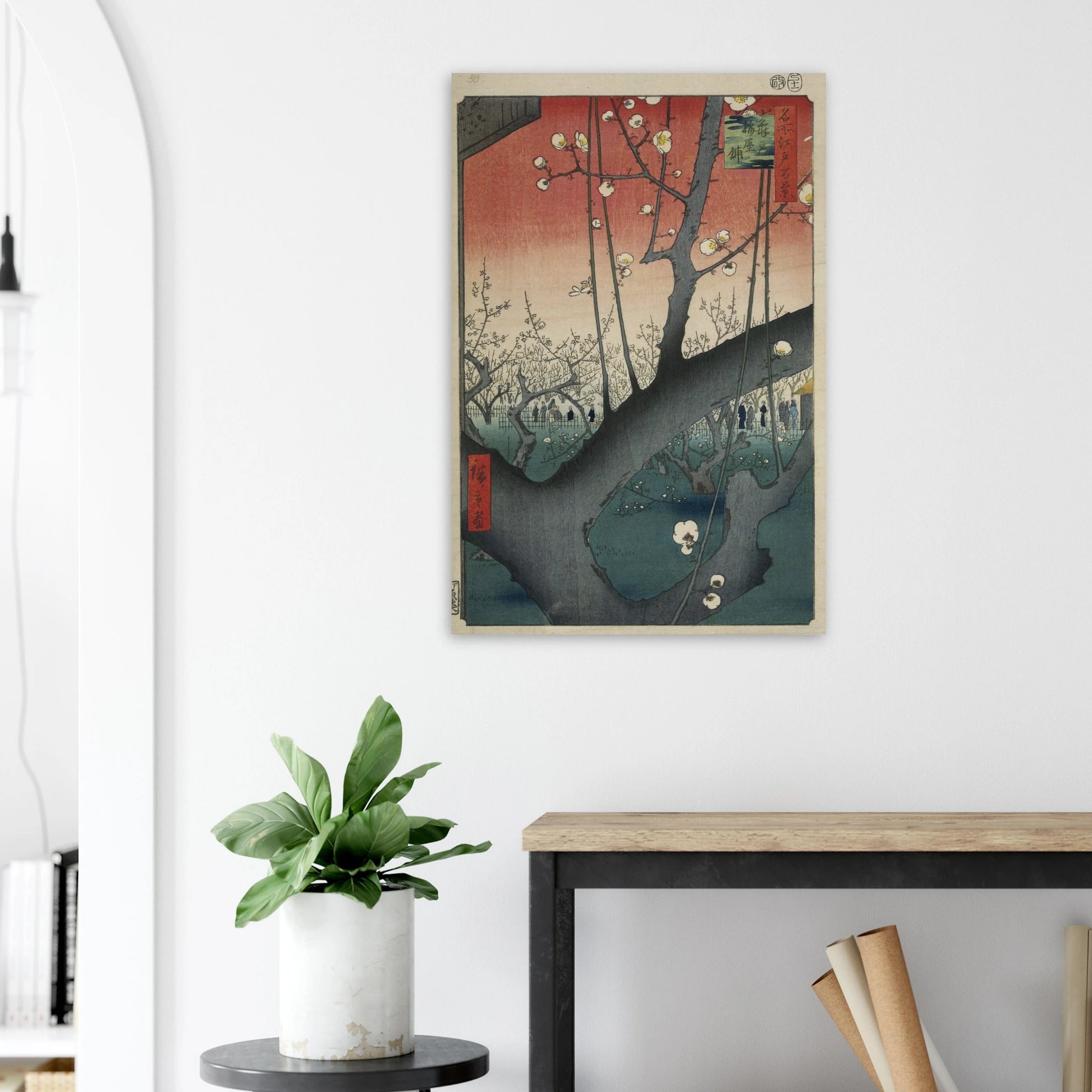 Framed artwork on a wall above a desk with a plant and books.