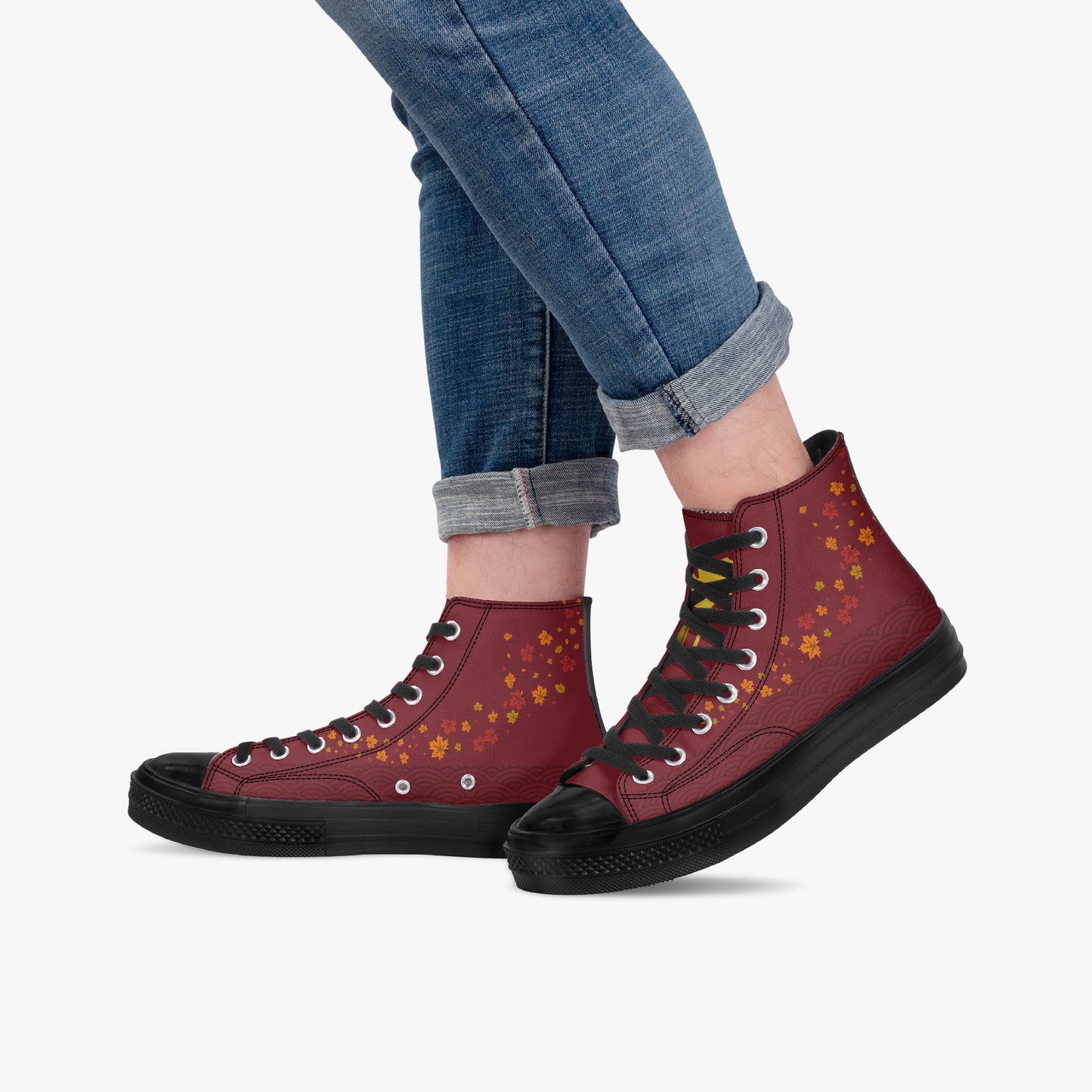A person wearing cuffed blue jeans and a pair of high-top burgundy sneakers with yellow floral patterns and black soles, shown against a light gray background.