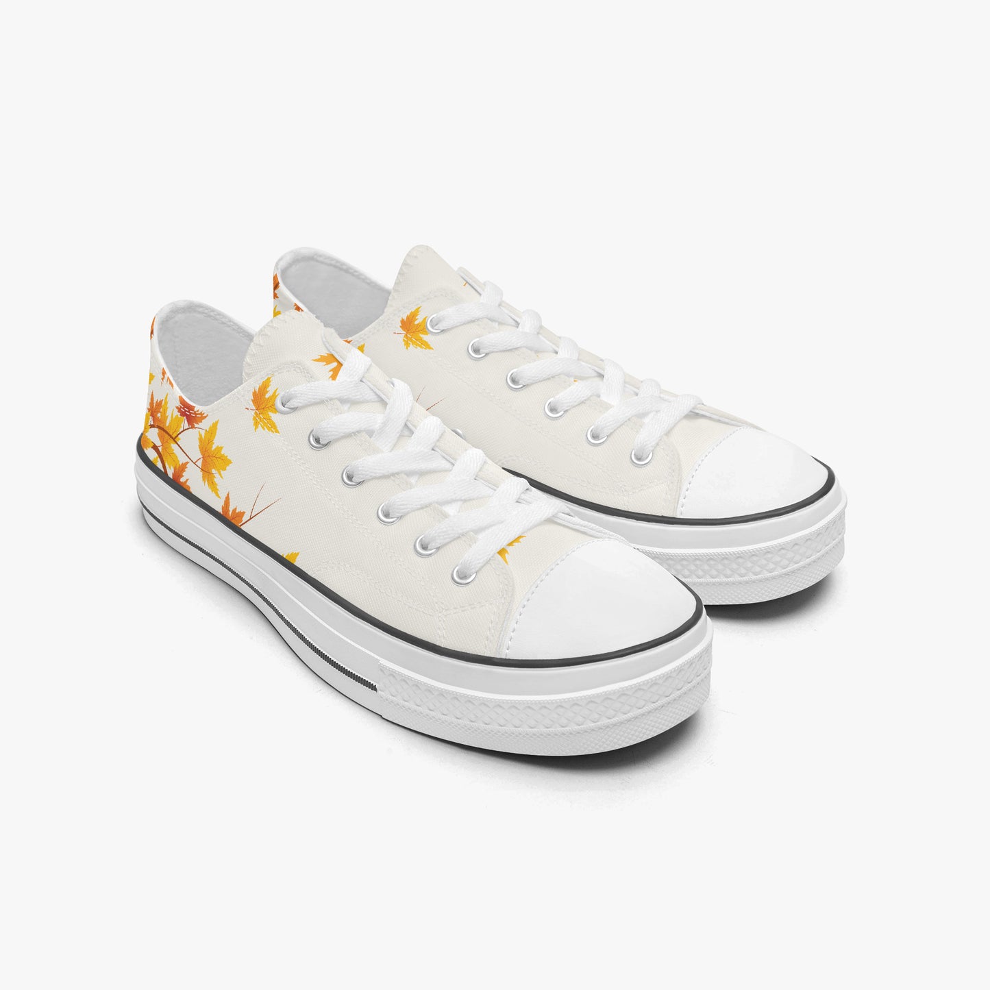 A pair of low-top canvas sneakers in off-white, decorated with a yellow-orange maple leaf pattern on the side and a black rubber trim around the toe and sole.