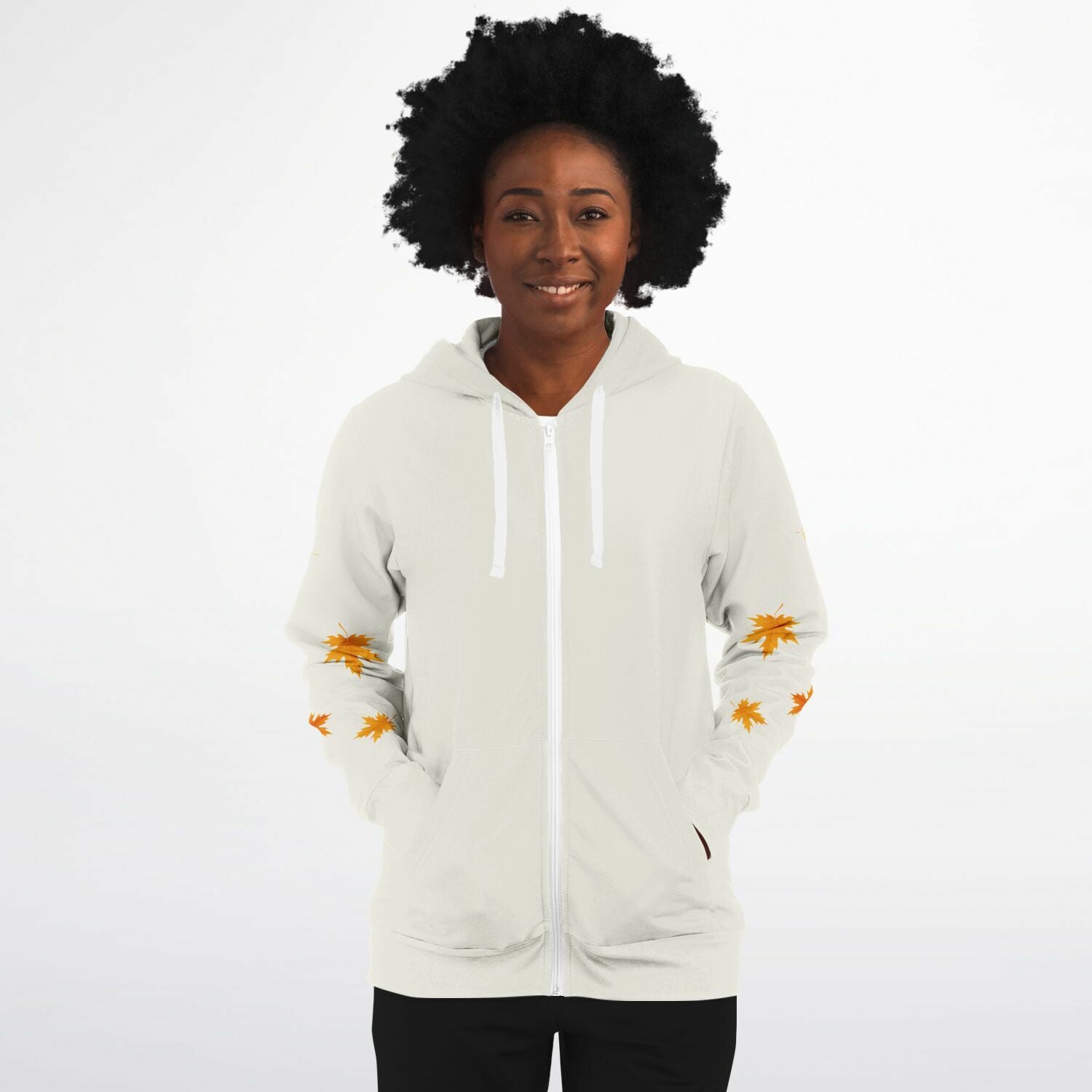 A woman with an afro hairstyle wearing a white zip-up hoodie with orange maple leaf prints on the sleeves, set against a plain white background.
