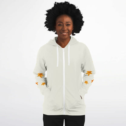 A woman with an afro hairstyle wearing a white zip-up hoodie with orange maple leaf prints on the sleeves, set against a plain white background.