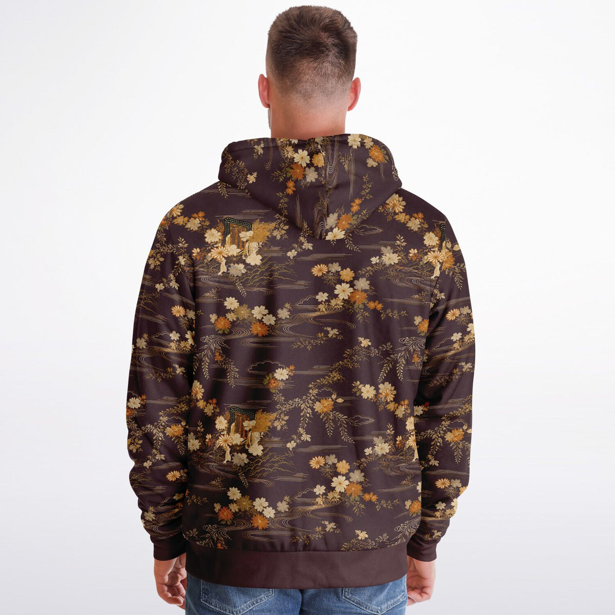A man viewed from behind wearing a dark brown hoodie with an all-over floral and branch pattern in beige, cream, and muted orange tones, paired with blue jeans against a plain white studio background.