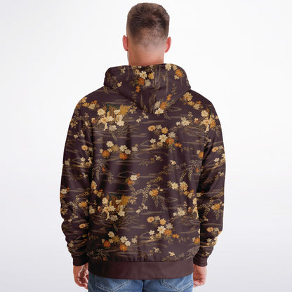 A man viewed from behind wearing a dark brown hoodie with an all-over floral and branch pattern in beige, cream, and muted orange tones, paired with blue jeans against a plain white studio background.