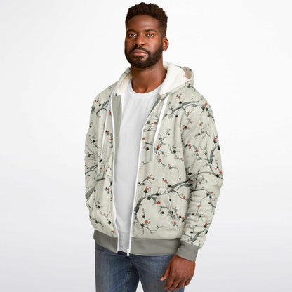 A man wearing a light beige hooded jacket with a gray and red cherry blossom branch pattern, layered over a white t-shirt and blue jeans, against a plain white background.