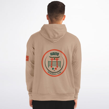 A man viewed from the back wearing a beige hoodie with a large circular graphic on the back reading 'HAITO PICKLEBALL CLUB' and a small red graphic on the left sleeve, against a plain light background.