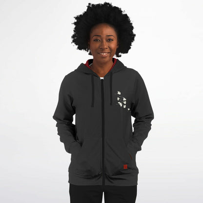 A woman with an afro hairstyle wearing a dark gray zip-up hoodie with a white graphic on the left chest, a red inner collar, and black pants, standing against a light gray background.