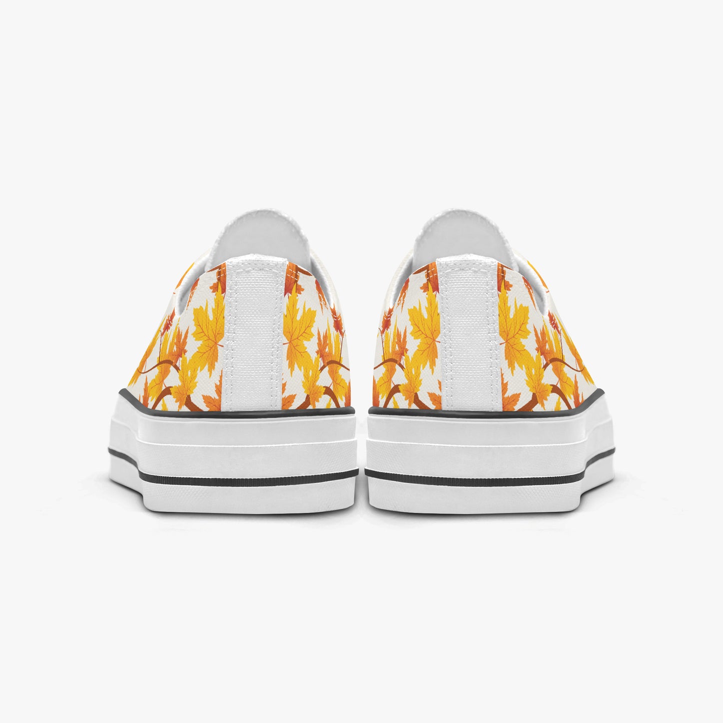 A pair of low-top canvas sneakers shown from the back, featuring a white background with a yellow and orange autumn leaf pattern on the sides and thick white platform soles with black stripes.