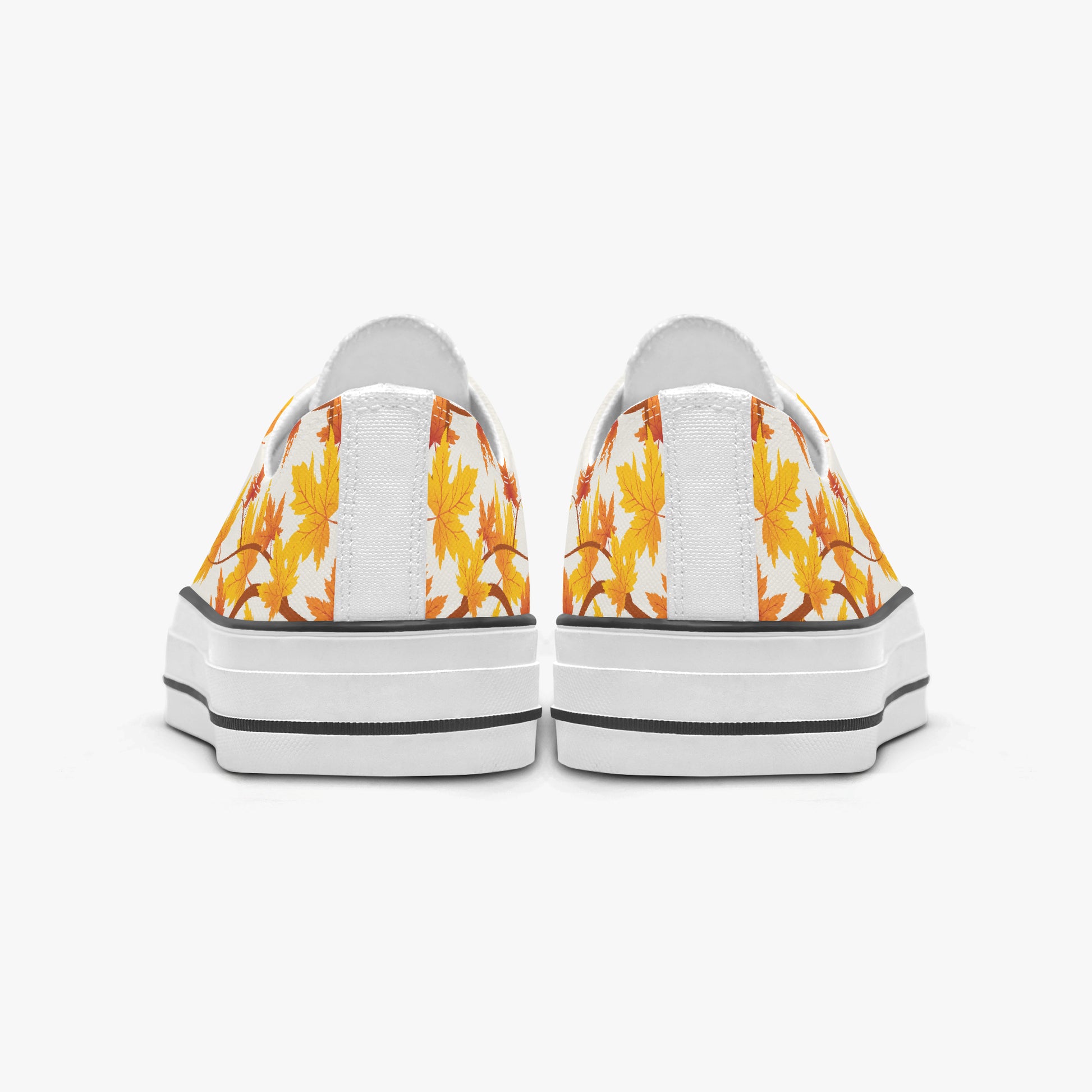 A pair of low-top canvas sneakers shown from the back, featuring a white background with a yellow and orange autumn leaf pattern on the sides and thick white platform soles with black stripes.