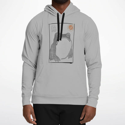 A man wearing a light gray pullover hoodie with a black and white graphic print of a frog on the chest, paired with black pants, against a plain white background.