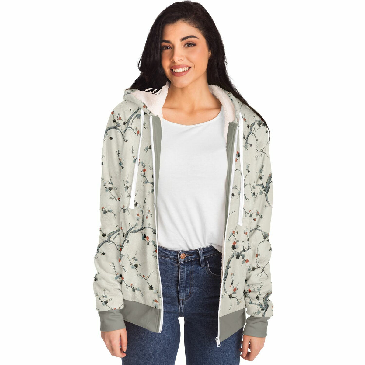 A woman modeling a light gray hooded sweatshirt with a delicate floral branch print, featuring a white fleece-lined hood, white drawstrings, and gray ribbed cuffs and hem, worn over a white t-shirt and blue jeans against a plain white background.