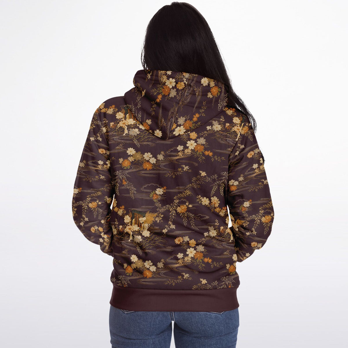 A woman viewed from behind wearing a dark brown hoodie with an all-over floral pattern in beige, cream, and muted orange, paired with blue jeans against a plain white studio background.