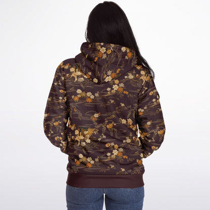 A woman viewed from behind wearing a dark brown hoodie with an all-over floral pattern in beige, cream, and muted orange, paired with blue jeans against a plain white studio background.