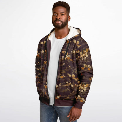A man wearing a dark brown and black floral patterned zip-up hoodie with a white hood lining, layered over a white t-shirt and blue jeans, against a plain white studio background.