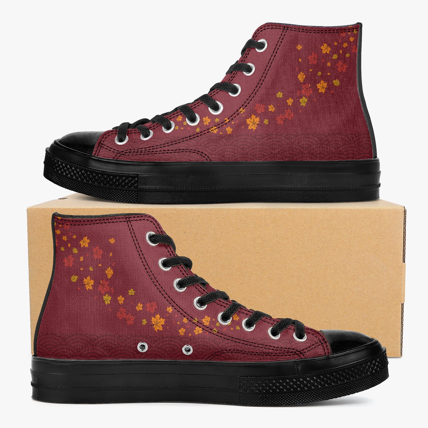 A pair of high-top canvas sneakers in burgundy with orange and yellow autumn leaf patterns, black soles, and black laces, displayed on a brown cardboard box against a light gray background.