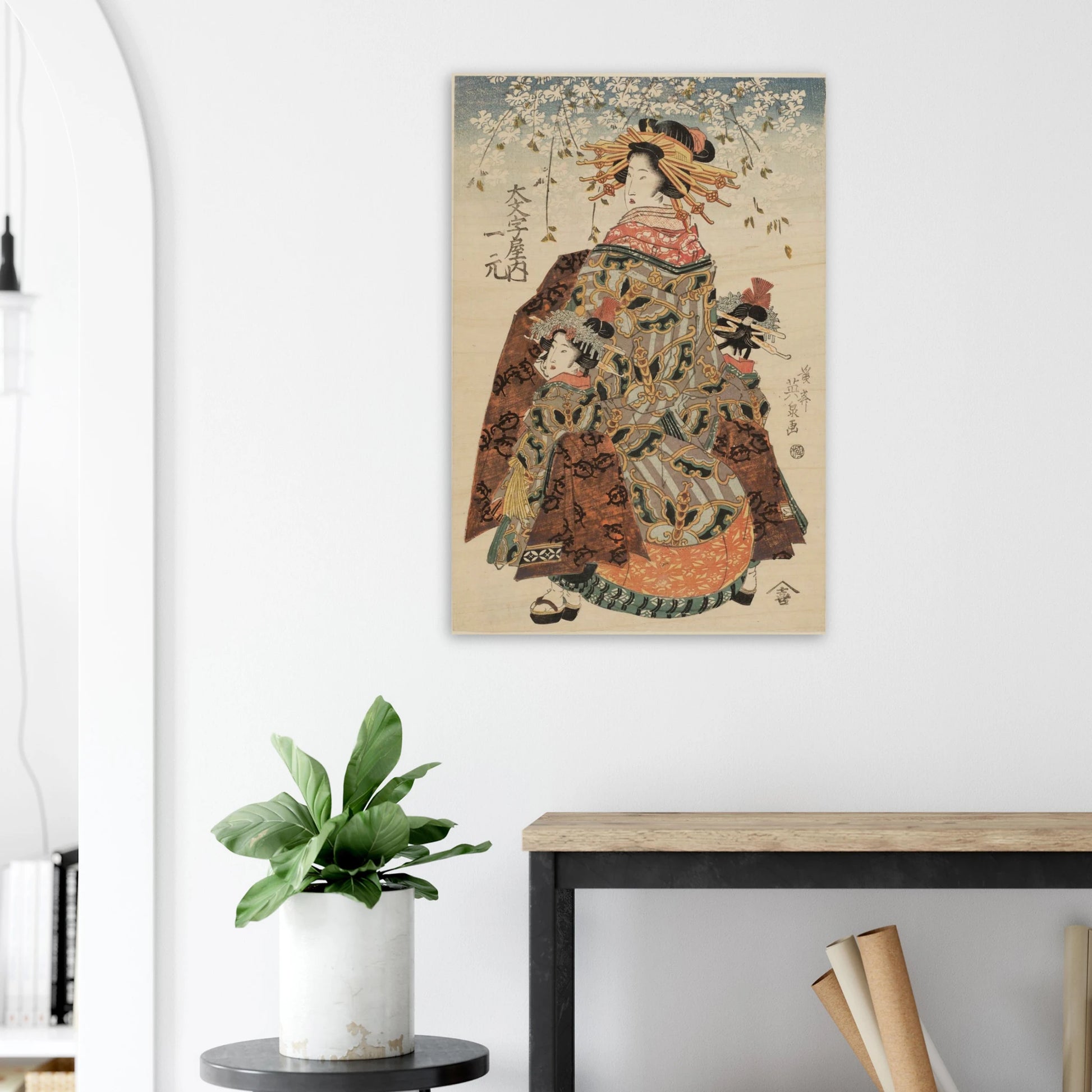Traditional Japanese artwork of a geisha on a wall above a desk with a plant and books.