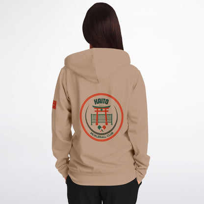 A woman viewed from the back wearing a beige hoodie with a large circular 'Haitio Pickleball Club' graphic on the back and a small red graphic on the left sleeve, set against a plain white background.
