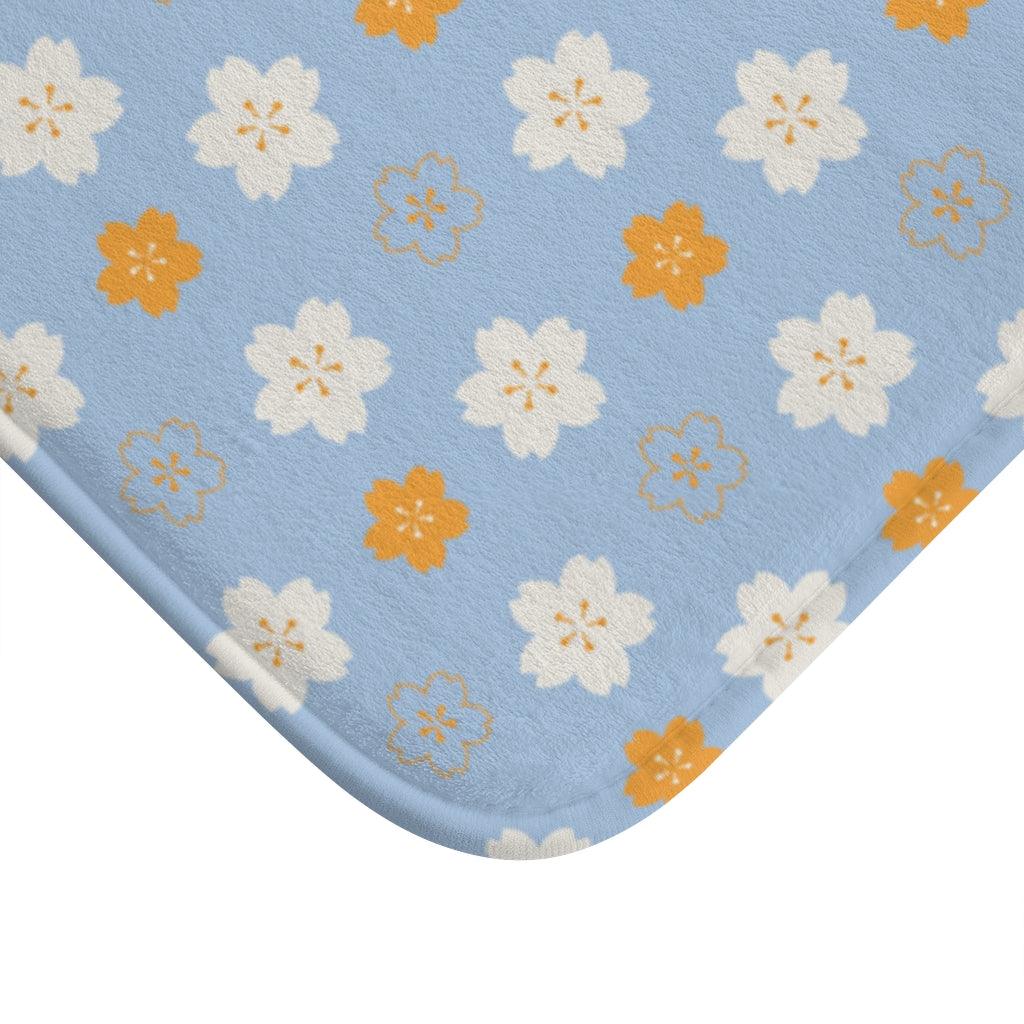 Orange and White Flower on Blue Origami Pattern Bath Mat.   Japanese style bathmats are the perfect finishing flourish for a stylish, personality-filled bathroom, and this bath mat is as practical, as it is stylish - the anti-slip backing keeps the bath mat firmly in place and reduces the risk of slipping. 100% Microfiber. Vibrant print exit in 2 sizes 34” x 21” (86 x 53 cm) or 24” x 17” (61 x 43 cm). Anti-slip backing. Binding around the edges. Machine wash cold, gentle cycle. Tumble dry low or line dry. 
